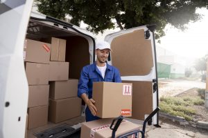 Delivery man holding a box next to a delivery van