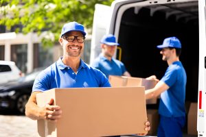 Efficient delivery men in blue uniforms are moving appliances into a truck
